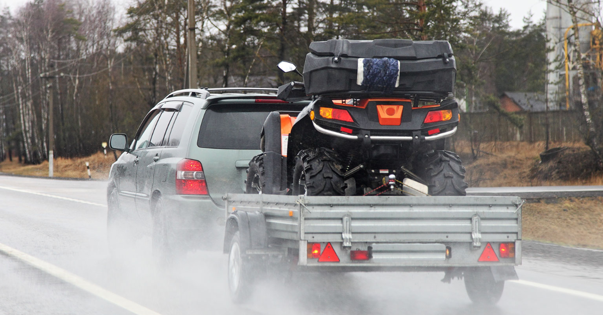 An SUV hauls a utility trailer in Albuquerque with an ATV loaded onto it.